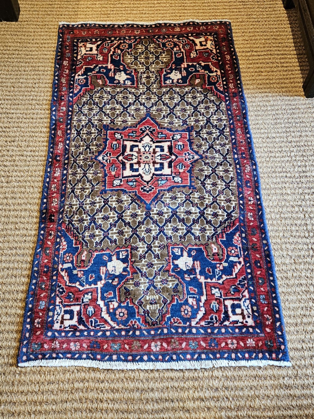A small rectangular hand-knotted wool rug featuring a central star medallion, geometric lattice field, and deep red and blue borders. View IV