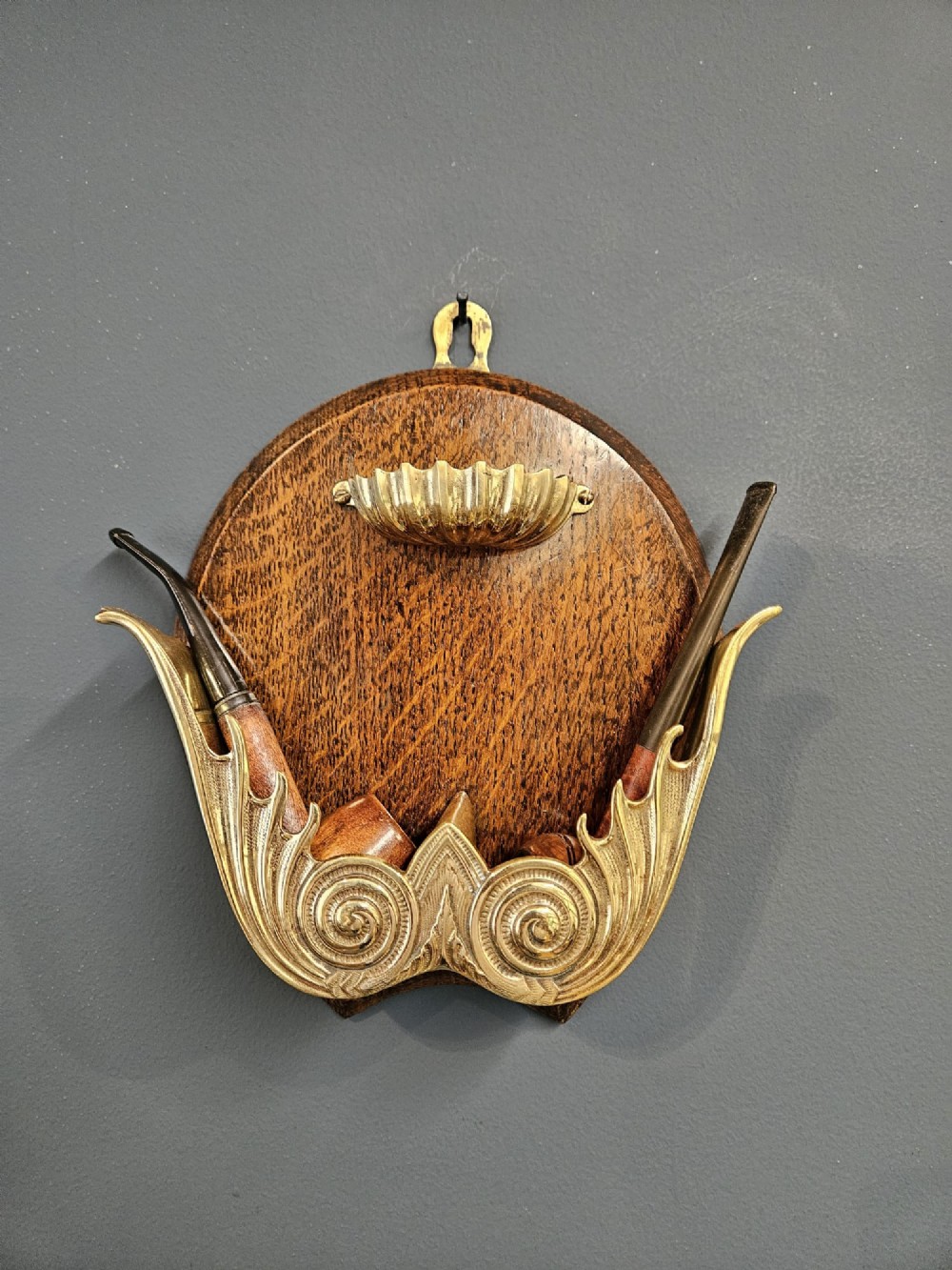A Victorian wall-mounted oak pipe rack featuring ornamental cast brass scrollwork holders and a brass shell motif. View II