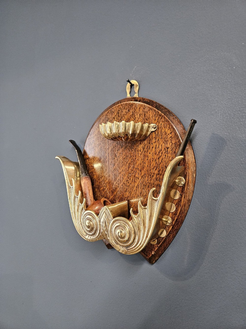A Victorian wall-mounted oak pipe rack featuring ornamental cast brass scrollwork holders and a brass shell motif. View IV