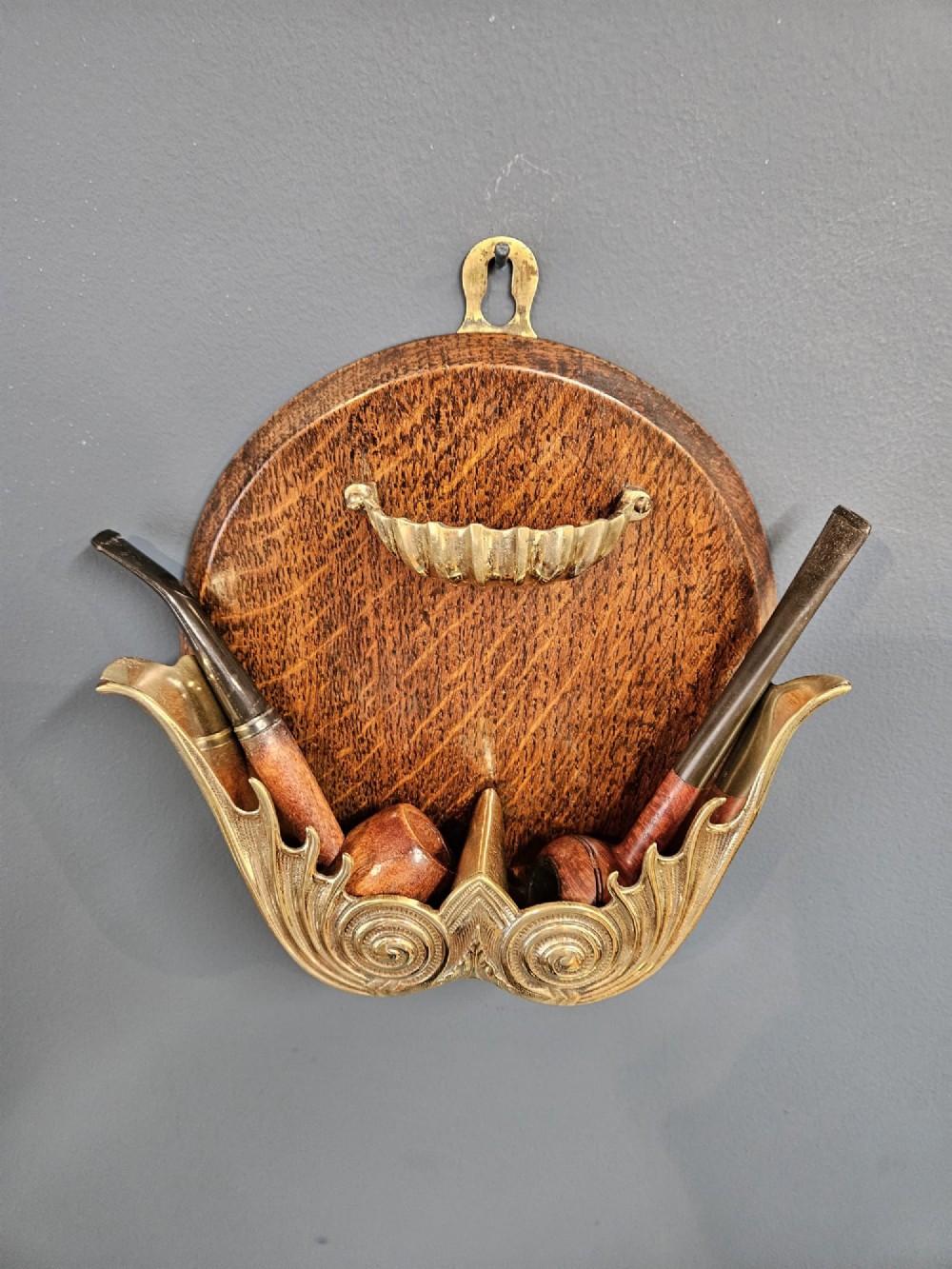A Victorian wall-mounted oak pipe rack featuring ornamental cast brass scrollwork holders and a brass shell motif. View V