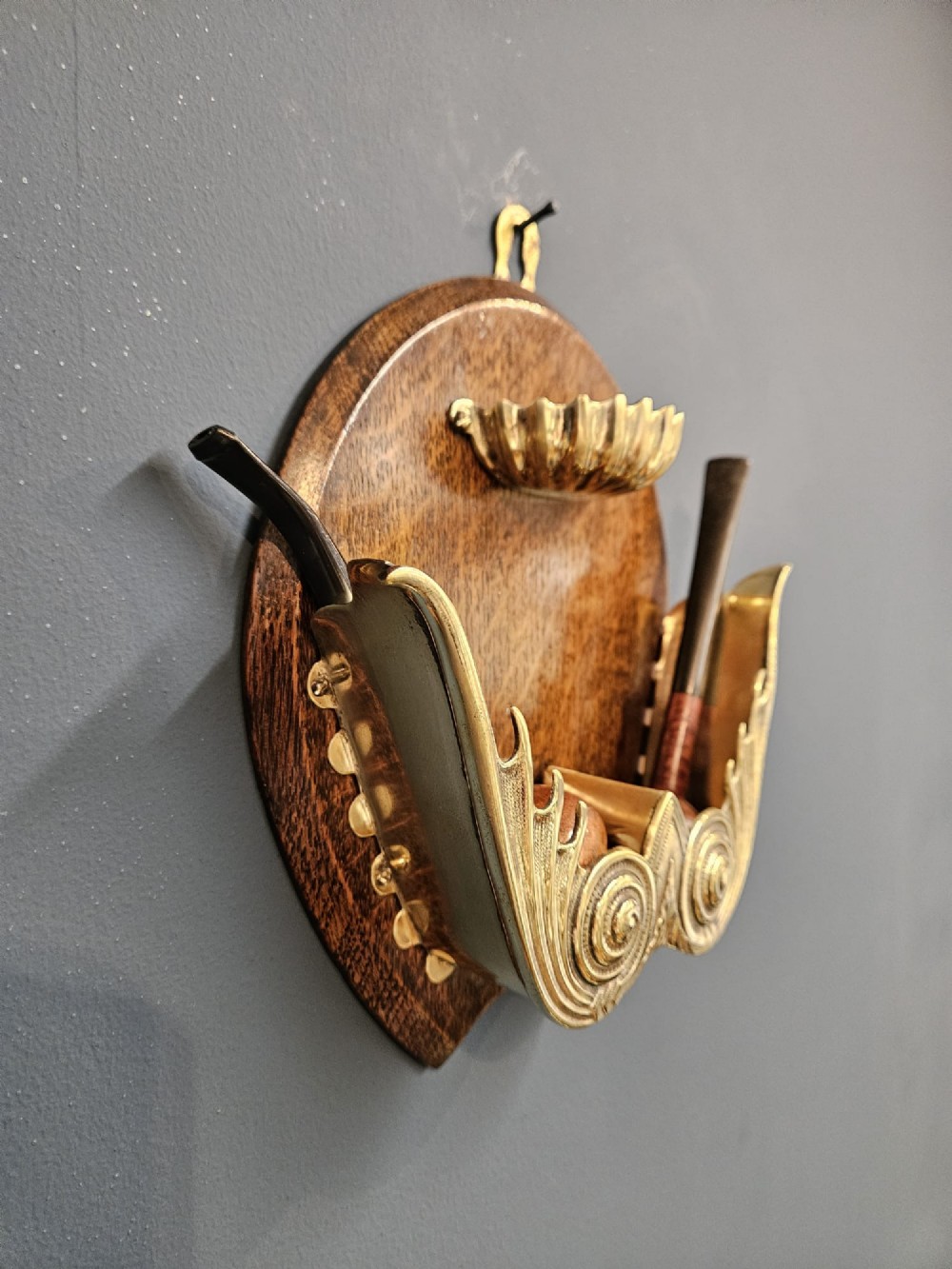 A Victorian wall-mounted oak pipe rack featuring ornamental cast brass scrollwork holders and a brass shell motif. View VI