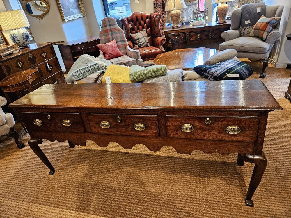A George II oak dresser base featuring three drawers, brass handles, a shaped apron, and four cabriole legs. View II