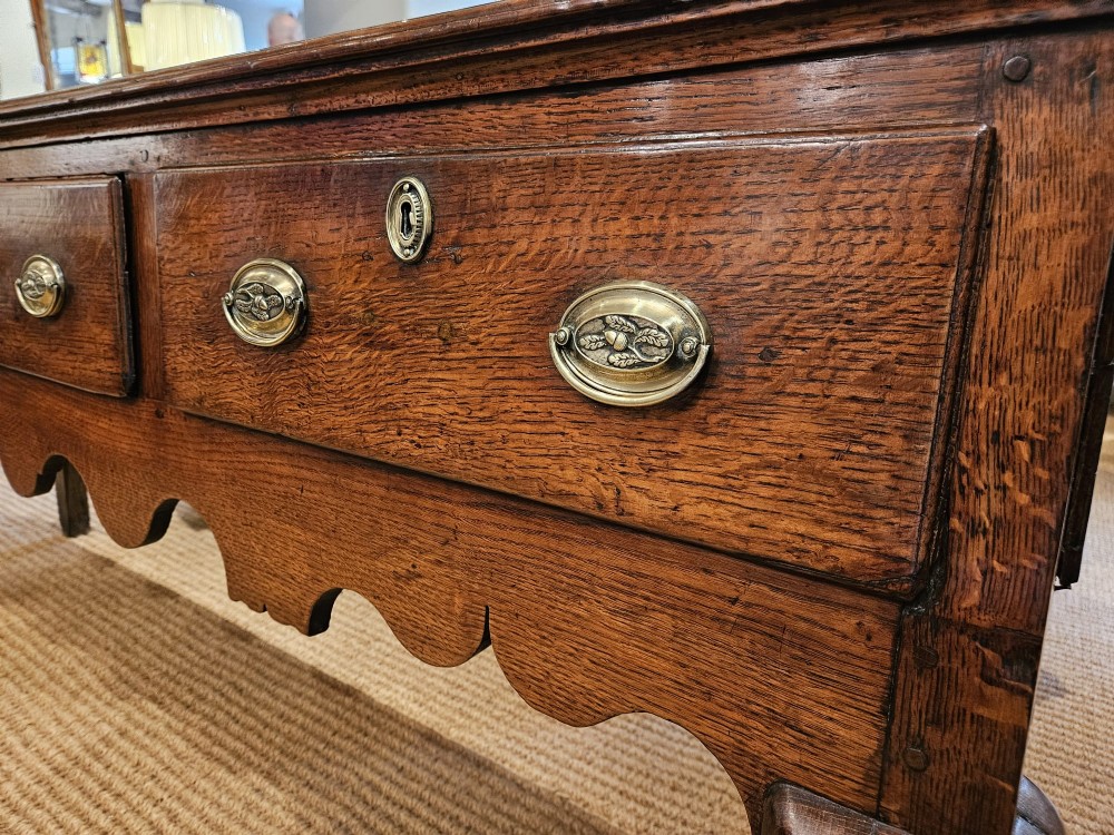 A George II oak dresser base featuring three drawers, brass handles, a shaped apron, and four cabriole legs. View III
