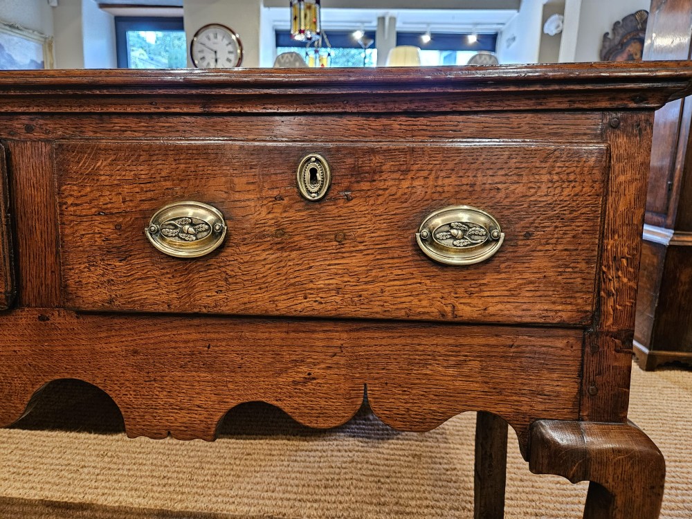 A George II oak dresser base featuring three drawers, brass handles, a shaped apron, and four cabriole legs. View V