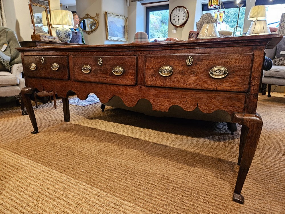 A George II oak dresser base featuring three drawers, brass handles, a shaped apron, and four cabriole legs. View VIII