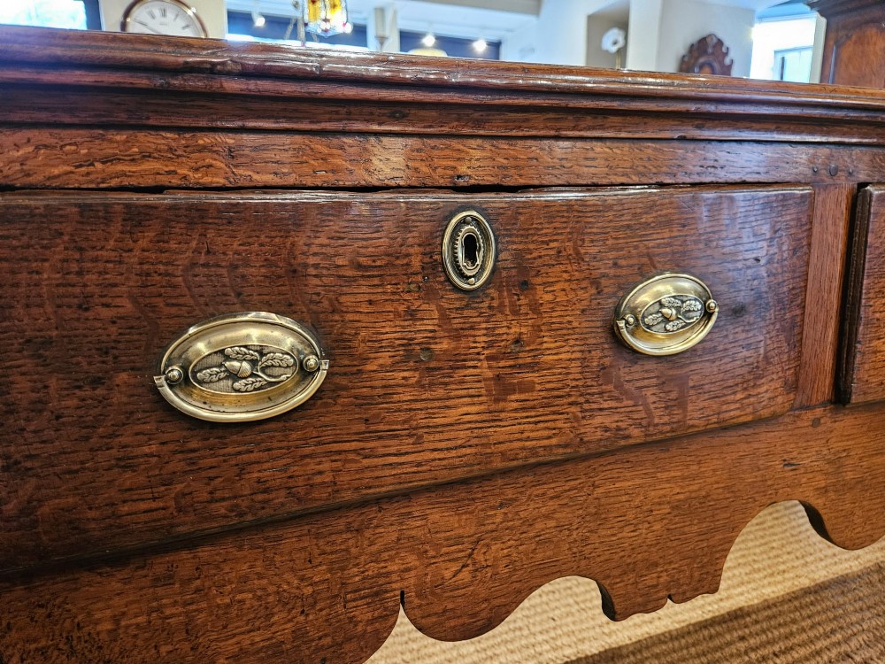 A George II oak dresser base featuring three drawers, brass handles, a shaped apron, and four cabriole legs. View XI