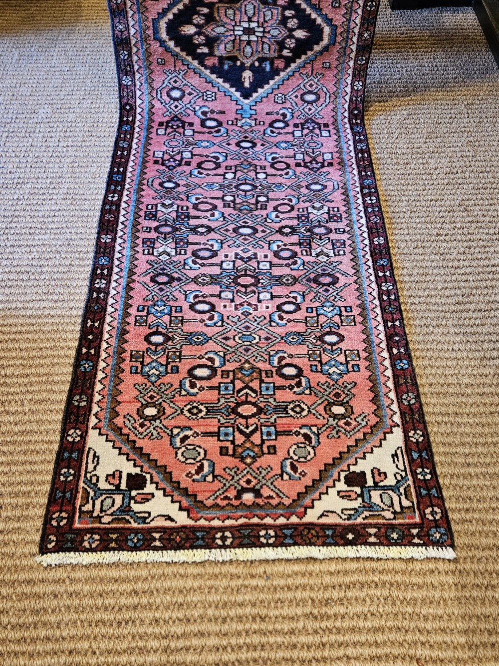 A long hand-knotted pure wool runner rug featuring geometric medallions in rose pink, navy blue, and cream. View VII