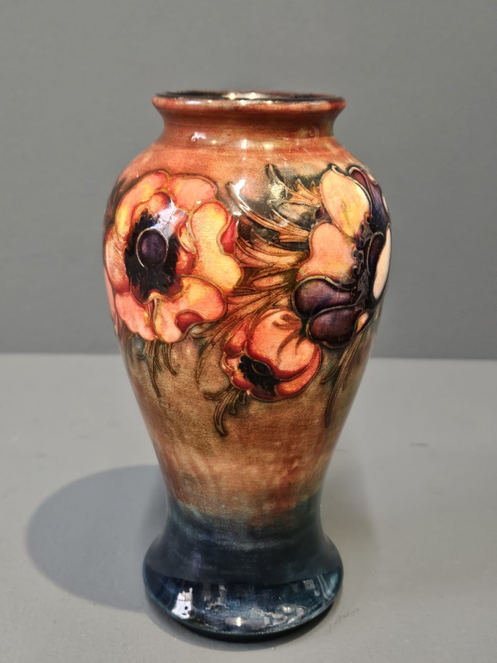 A baluster-shaped ceramic vase featuring hand-painted tubelined anemone flowers over a rich red flambe glaze background. View II