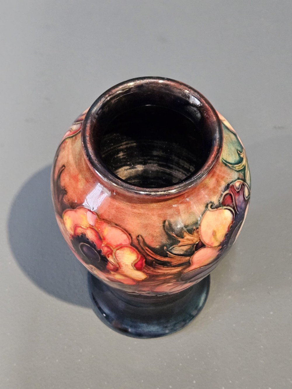A baluster-shaped ceramic vase featuring hand-painted tubelined anemone flowers over a rich red flambe glaze background. View III