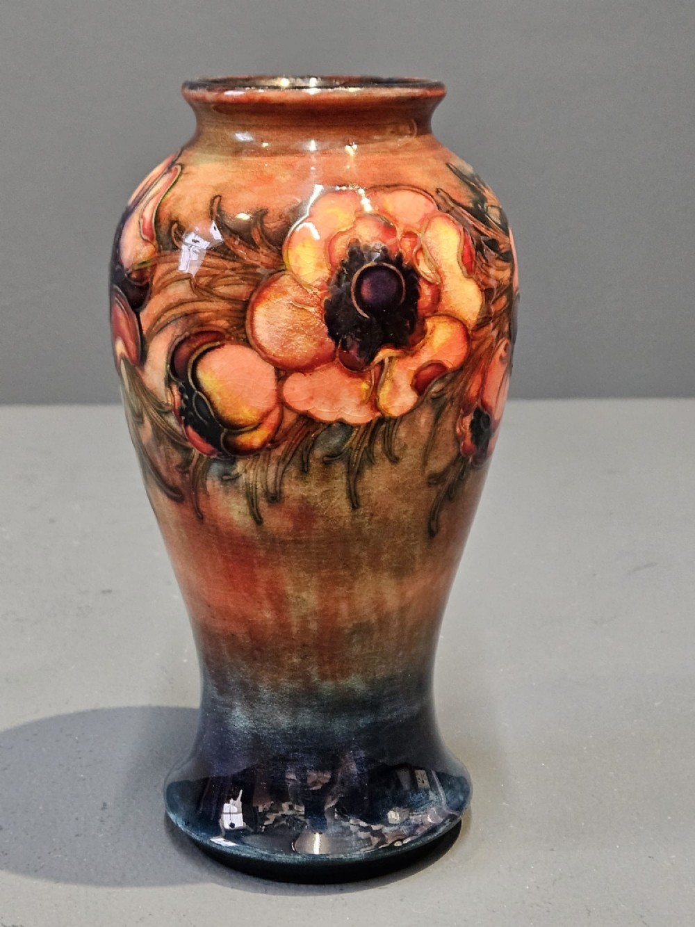 A baluster-shaped ceramic vase featuring hand-painted tubelined anemone flowers over a rich red flambe glaze background. View V