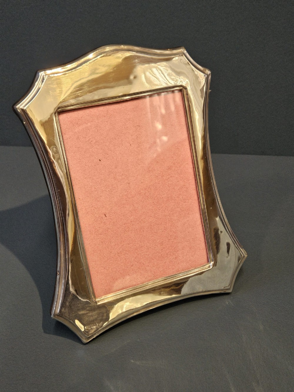 An Edwardian sterling silver photo frame featuring swept concave sides, a shaped crest, polished silver surface, and portrait orientation.
