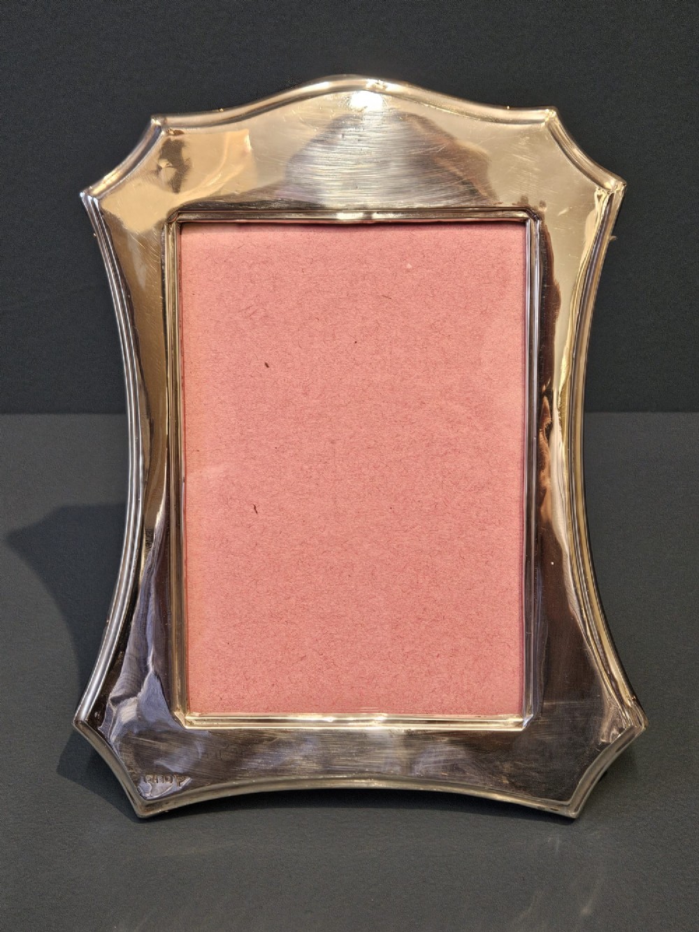 An Edwardian sterling silver photo frame featuring swept concave sides, a shaped crest, polished silver surface, and portrait orientation. View III