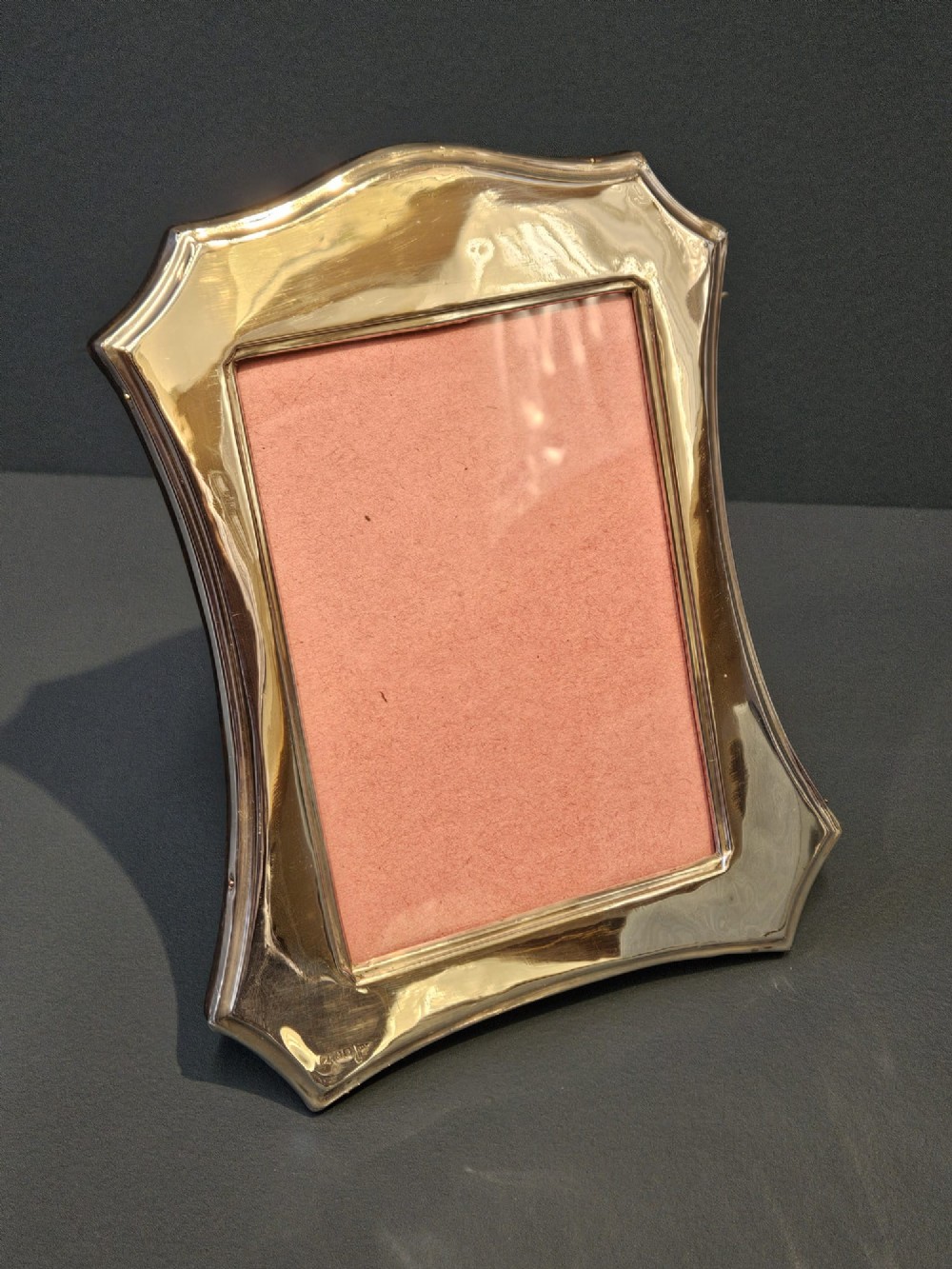 An Edwardian sterling silver photo frame featuring swept concave sides, a shaped crest, polished silver surface, and portrait orientation. View IV