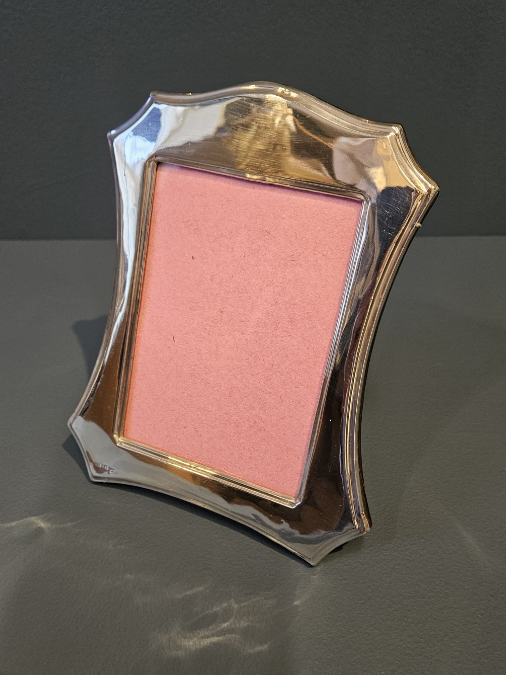 An Edwardian sterling silver photo frame featuring swept concave sides, a shaped crest, polished silver surface, and portrait orientation. View V