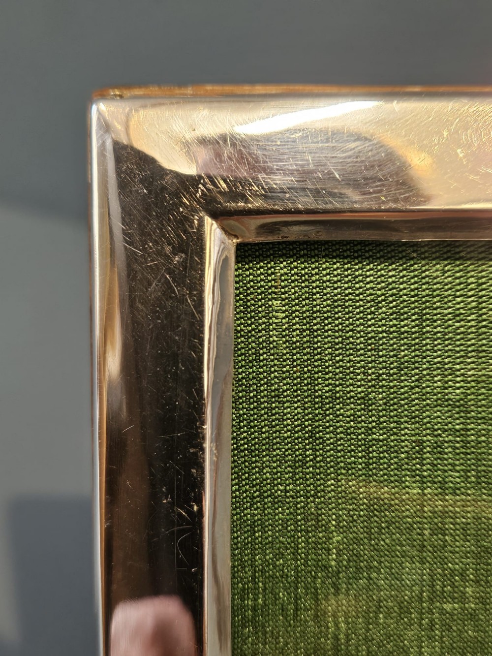 A rectangular George V silver photo frame with a plain polished border and a green fabric insert resting on a neutral surface. View III