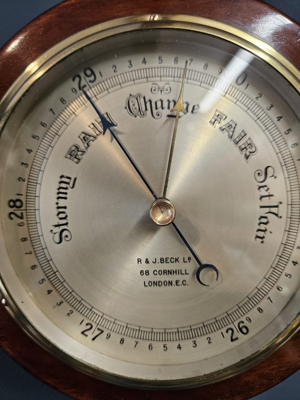 A circular Victorian aneroid barometer set within a polished mahogany surround with an engraved brass dial face and brass bezel. View IV