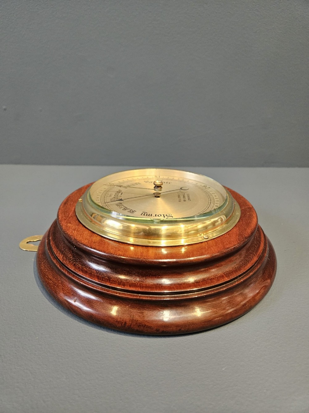 A circular Victorian aneroid barometer set within a polished mahogany surround with an engraved brass dial face and brass bezel. View V