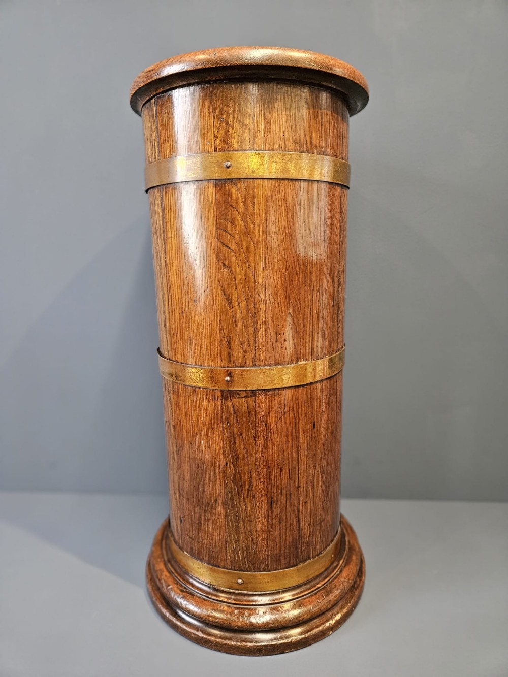 A cylindrical Victorian oak stick stand featuring polished brass binding straps and a moulded circular base.