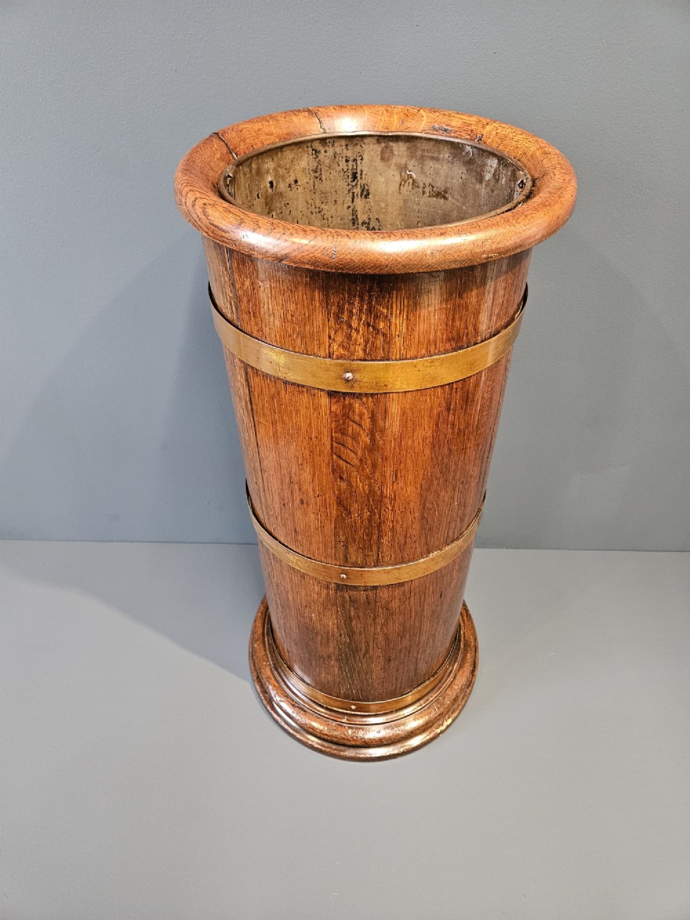 A cylindrical Victorian oak stick stand featuring polished brass binding straps and a moulded circular base. View II