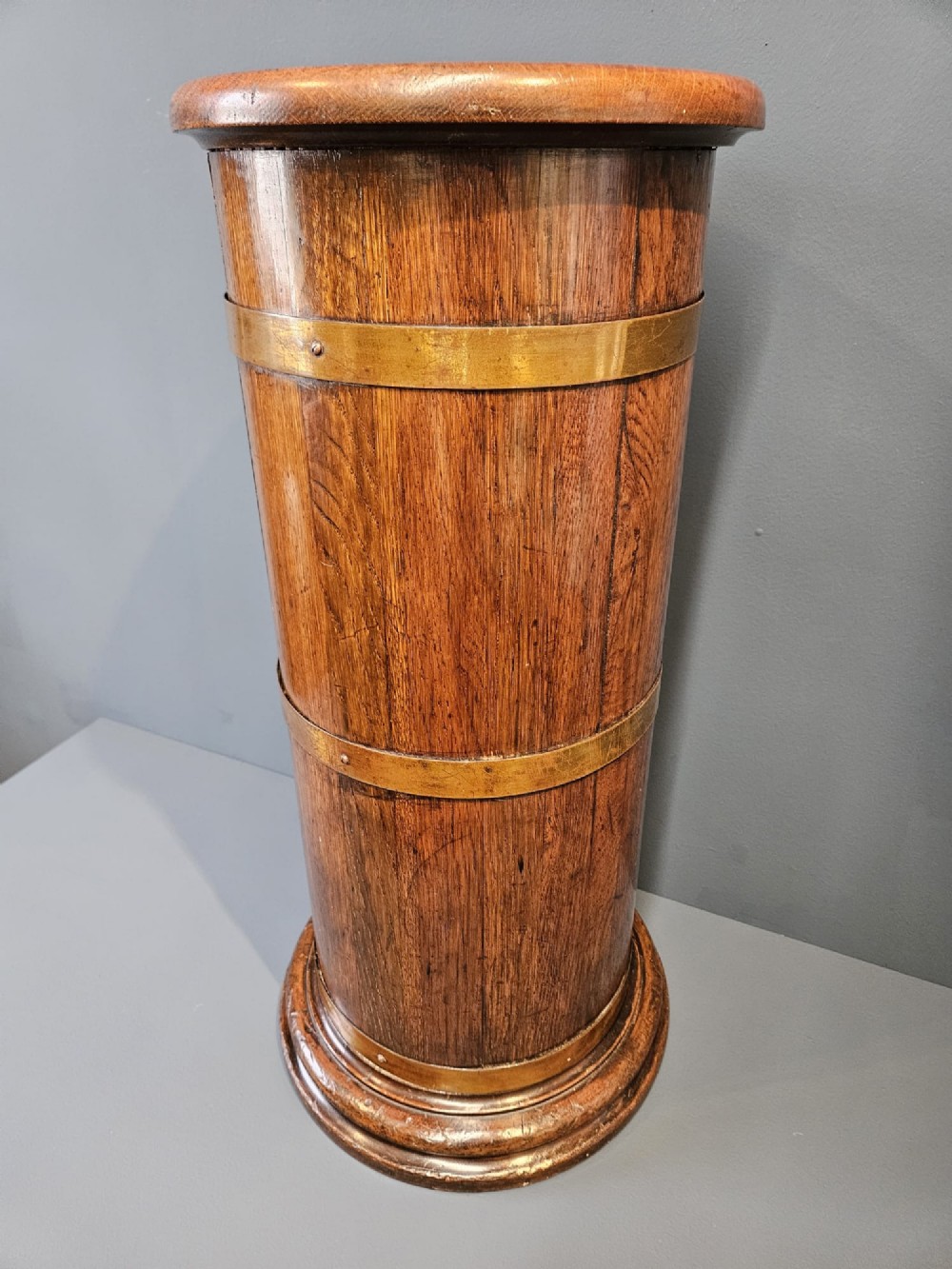 A cylindrical Victorian oak stick stand featuring polished brass binding straps and a moulded circular base. View III