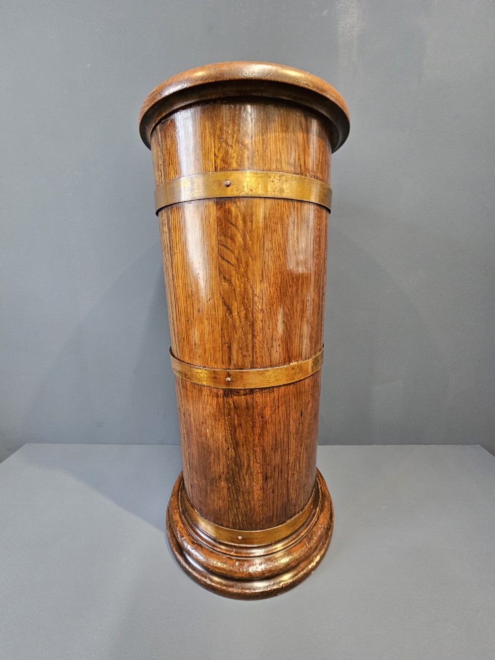 A cylindrical Victorian oak stick stand featuring polished brass binding straps and a moulded circular base. View IV