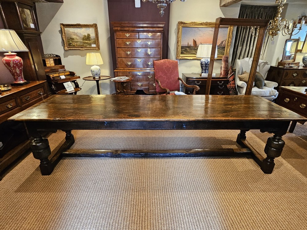 A long George II dark oak refectory dining table featuring a solid plank top, turned legs, and low stretcher rails.