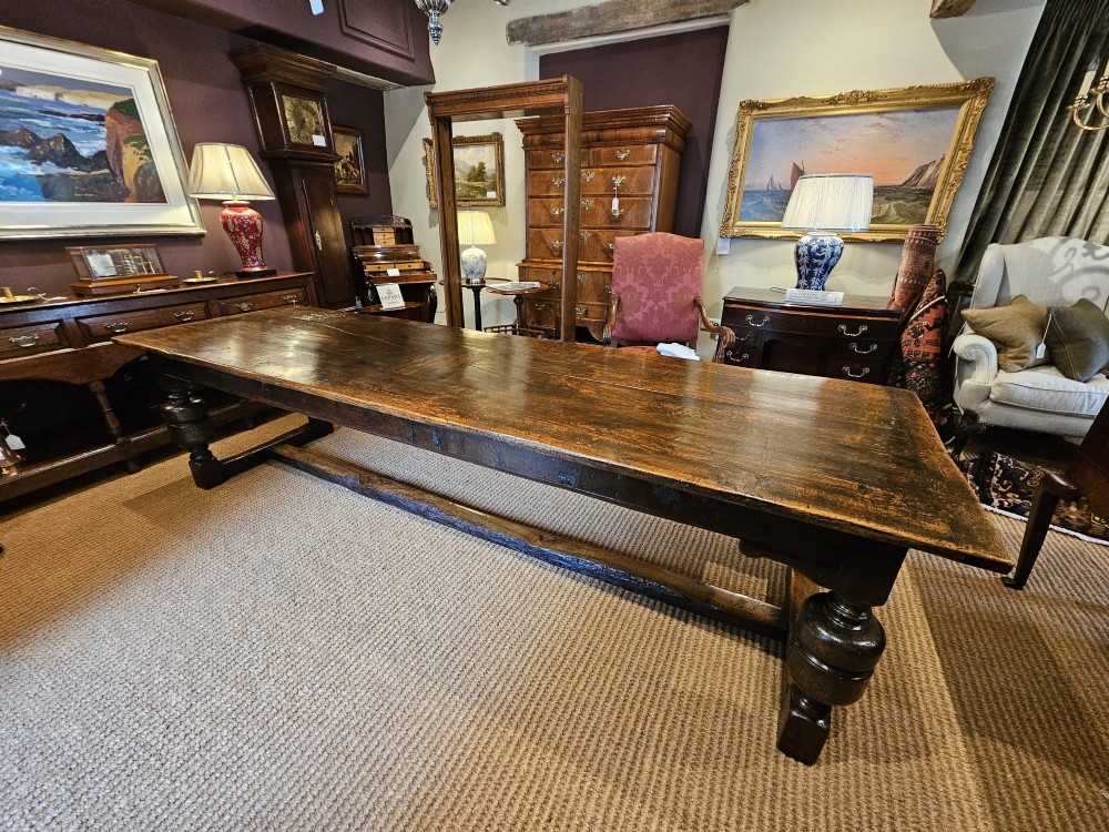 A long George II dark oak refectory dining table featuring a solid plank top, turned legs, and low stretcher rails. View II