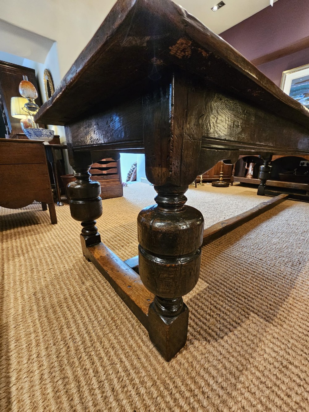 A long George II dark oak refectory dining table featuring a solid plank top, turned legs, and low stretcher rails. View III