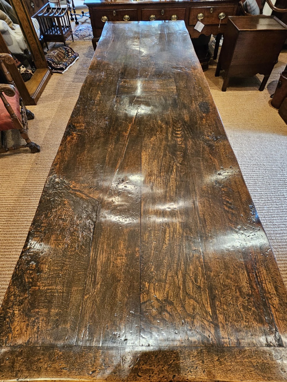 A long George II dark oak refectory dining table featuring a solid plank top, turned legs, and low stretcher rails. View IV