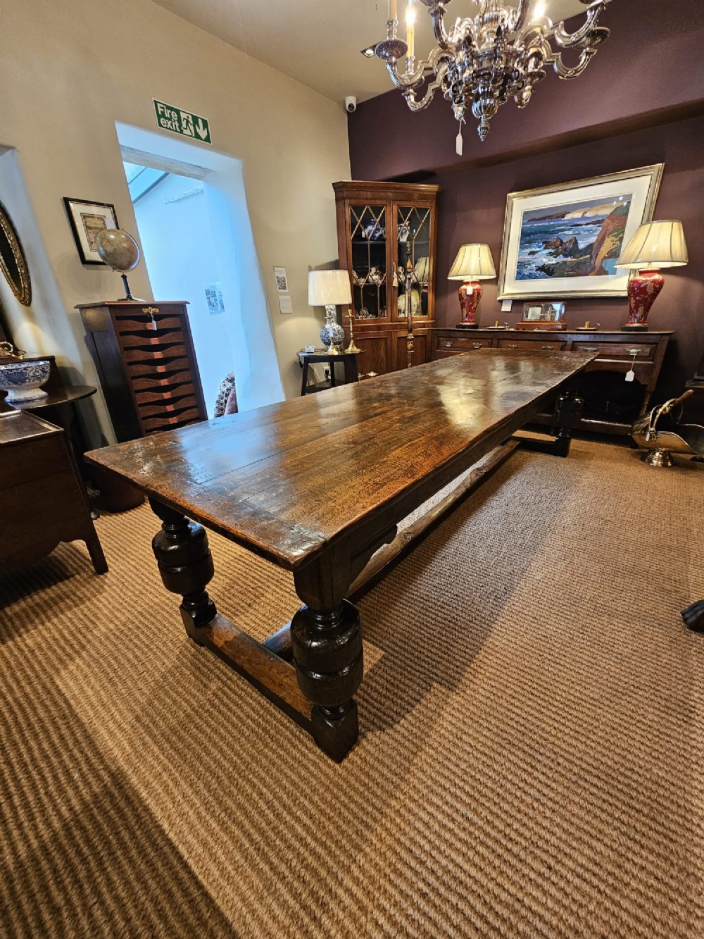 A long George II dark oak refectory dining table featuring a solid plank top, turned legs, and low stretcher rails. View V