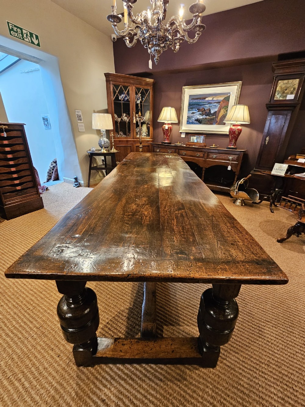 A long George II dark oak refectory dining table featuring a solid plank top, turned legs, and low stretcher rails. View VI