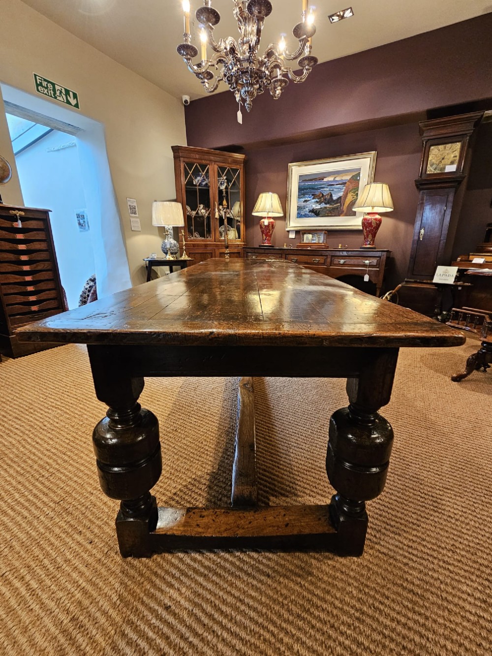 A long George II dark oak refectory dining table featuring a solid plank top, turned legs, and low stretcher rails. View VII