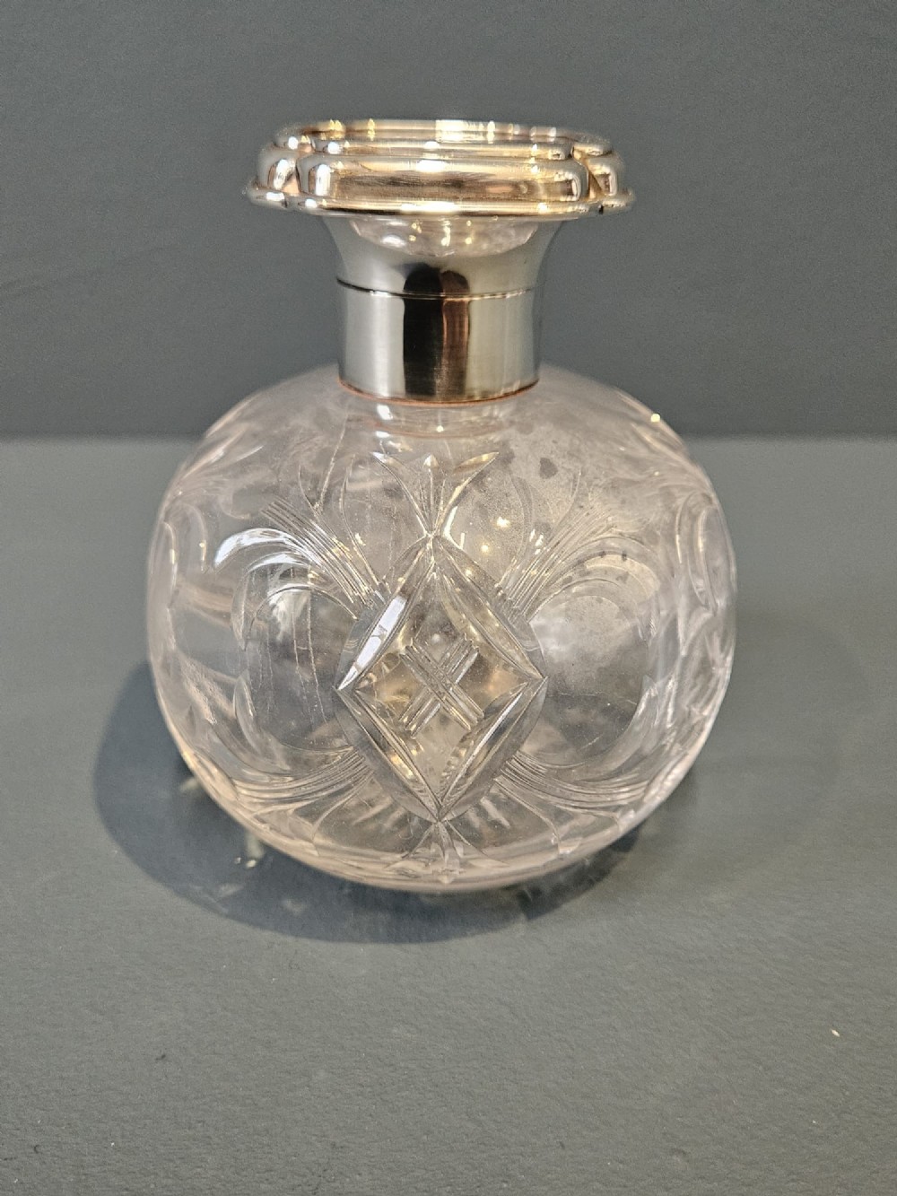 A round cut crystal glass scent bottle with a sterling silver neck collar and a square hinged silver lid featuring an inlaid tortoiseshell top. View II