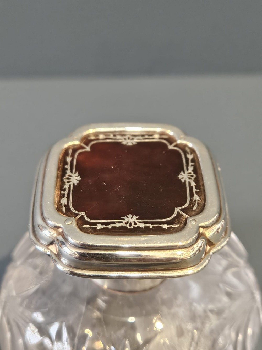 A round cut crystal glass scent bottle with a sterling silver neck collar and a square hinged silver lid featuring an inlaid tortoiseshell top. View IV
