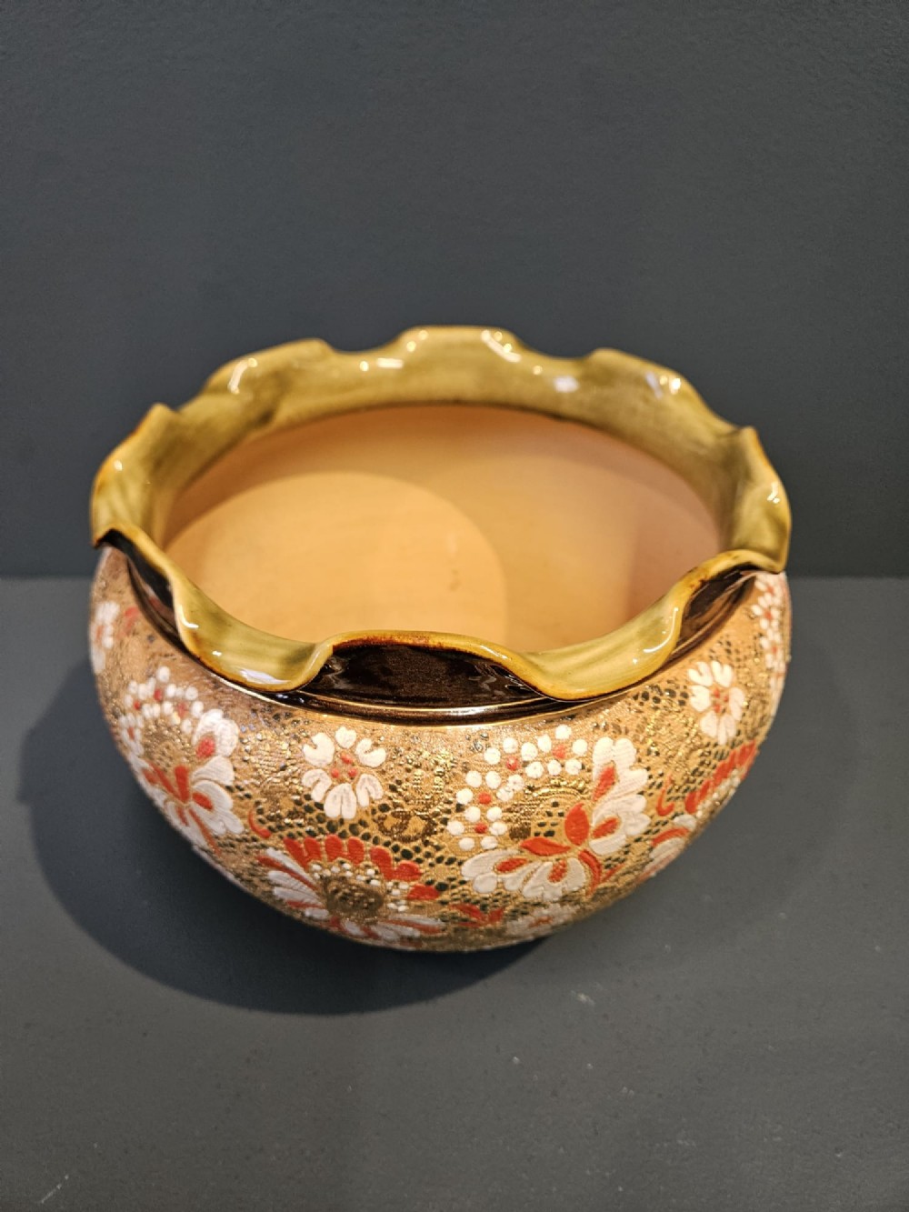 A Victorian Doulton Lambeth stoneware jardiniere featuring a wavy crimped rim, textured lace-impressed floral pattern in white and terracotta red on an ochre ground, and a dark brown upper band. View II