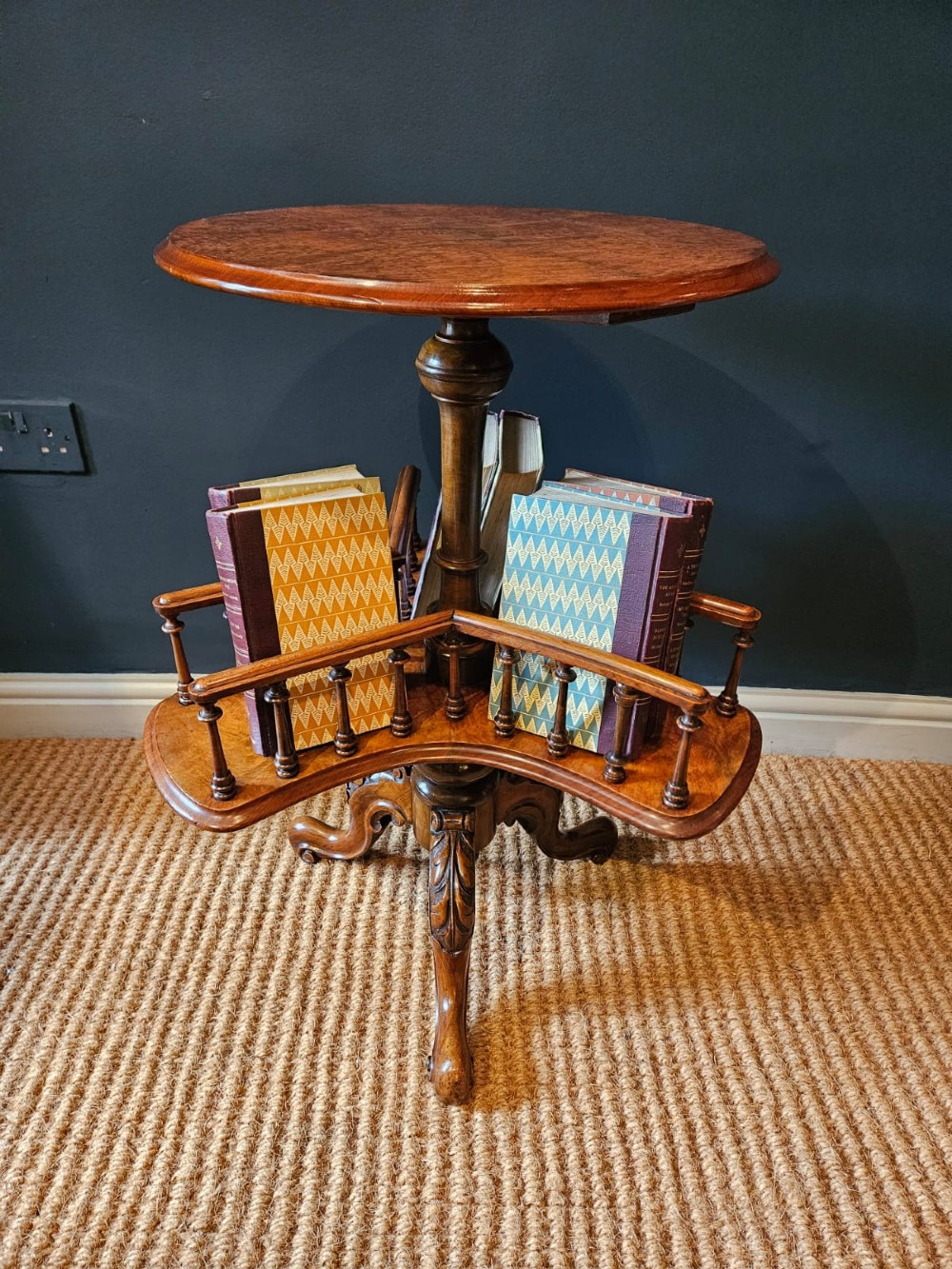 A Victorian burr walnut revolving book table with a round top, three spindle-railed book compartments, a turned central stem, and carved tripod legs. View III