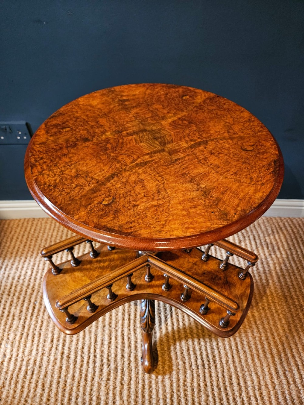 A Victorian burr walnut revolving book table with a round top, three spindle-railed book compartments, a turned central stem, and carved tripod legs. View V