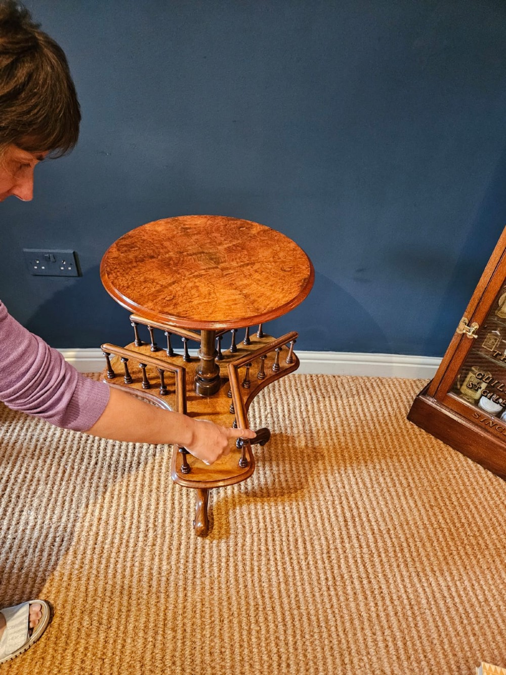 A Victorian burr walnut revolving book table with a round top, three spindle-railed book compartments, a turned central stem, and carved tripod legs. View VI