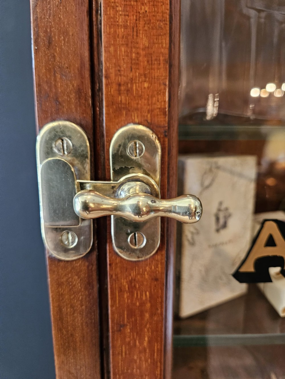 A tall Edwardian mahogany glazed display cabinet featuring gilded commercial typography on the glass door and shelves filled with apothecary bottles and packages. View IV