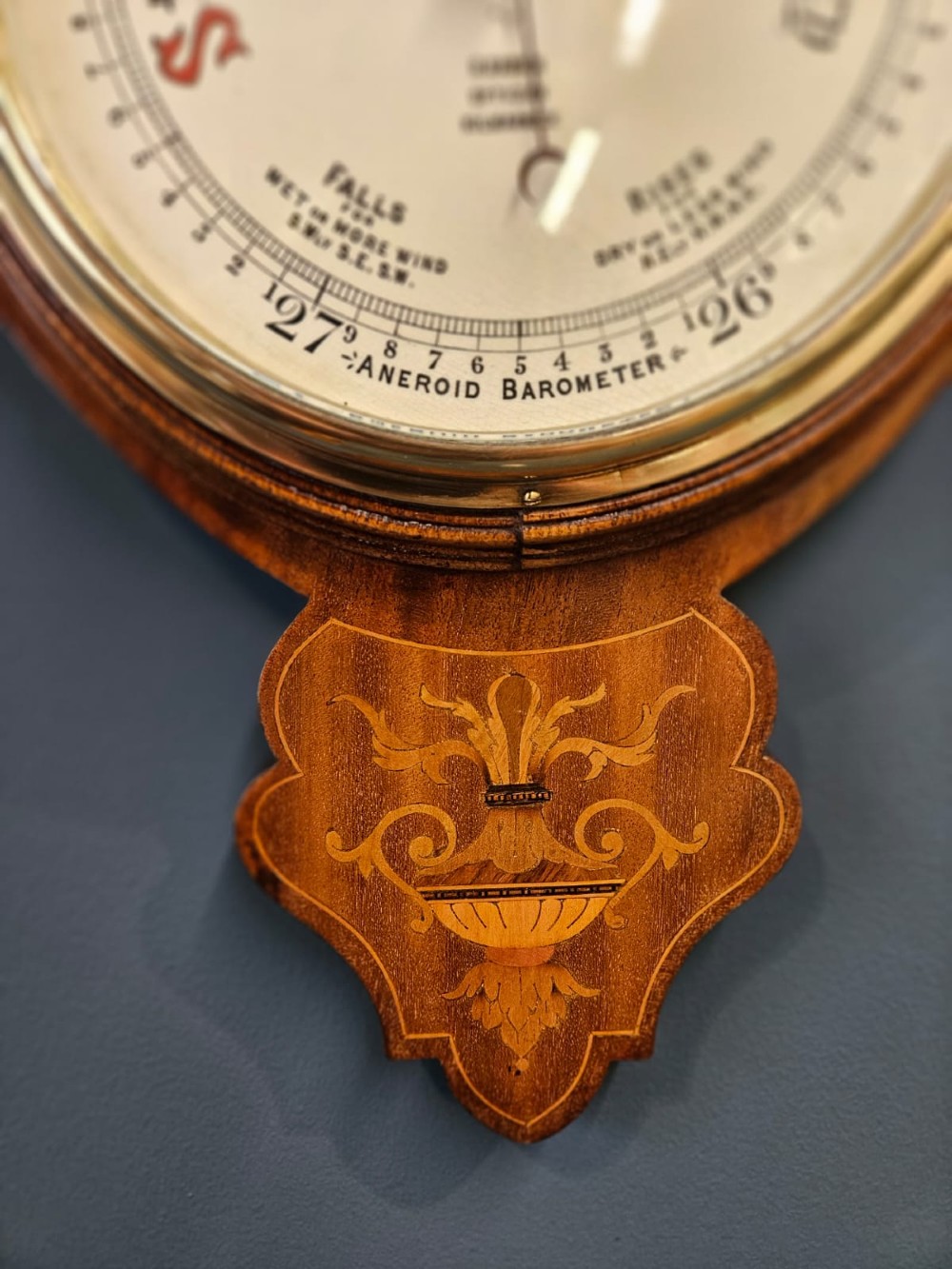 An Edwardian mahogany banjo barometer featuring decorative satinwood urn inlays, an upper thermometer gauge, and a circular aneroid pressure dial. View II