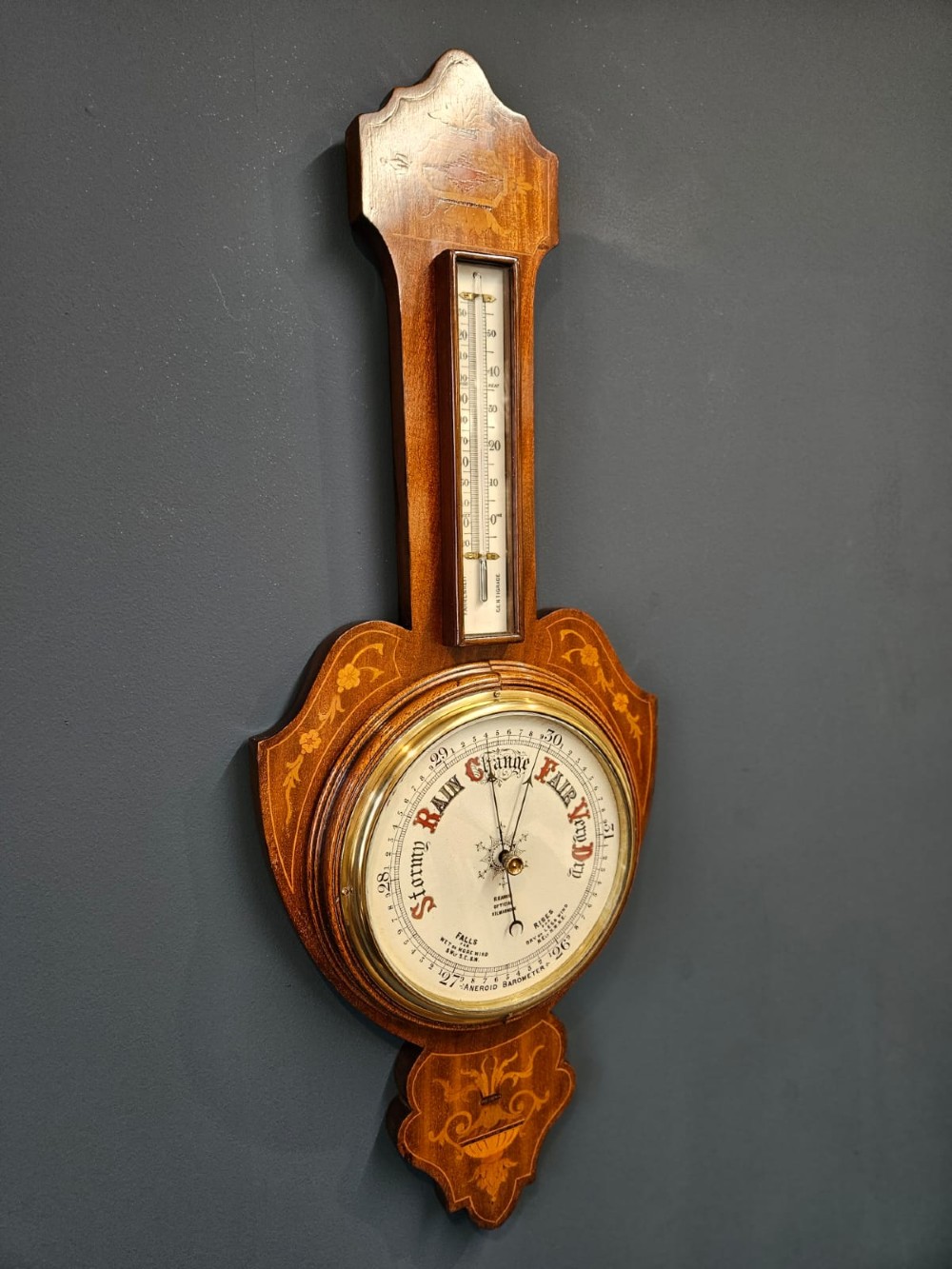 An Edwardian mahogany banjo barometer featuring decorative satinwood urn inlays, an upper thermometer gauge, and a circular aneroid pressure dial. View V
