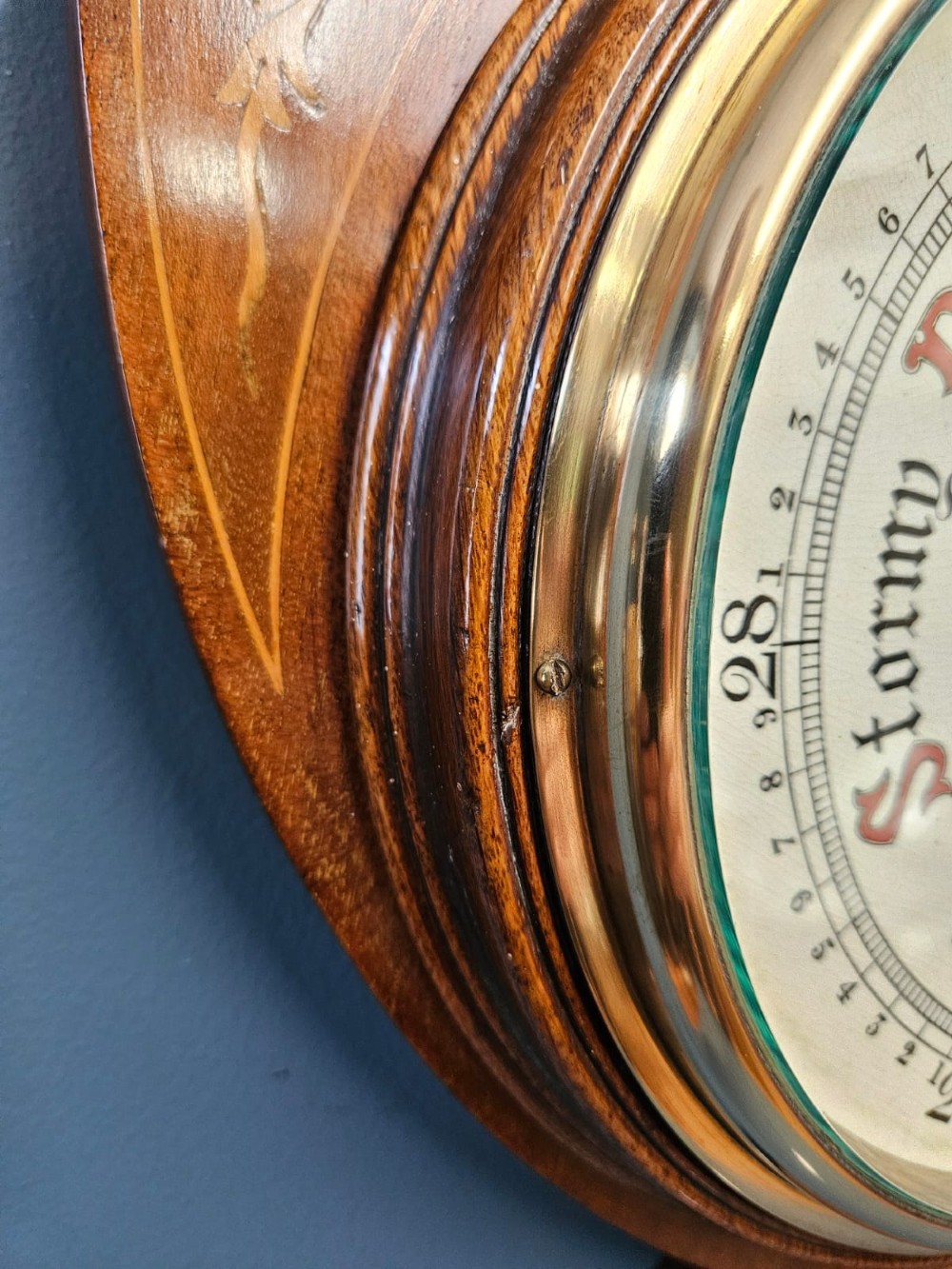 An Edwardian mahogany banjo barometer featuring decorative satinwood urn inlays, an upper thermometer gauge, and a circular aneroid pressure dial. View VII