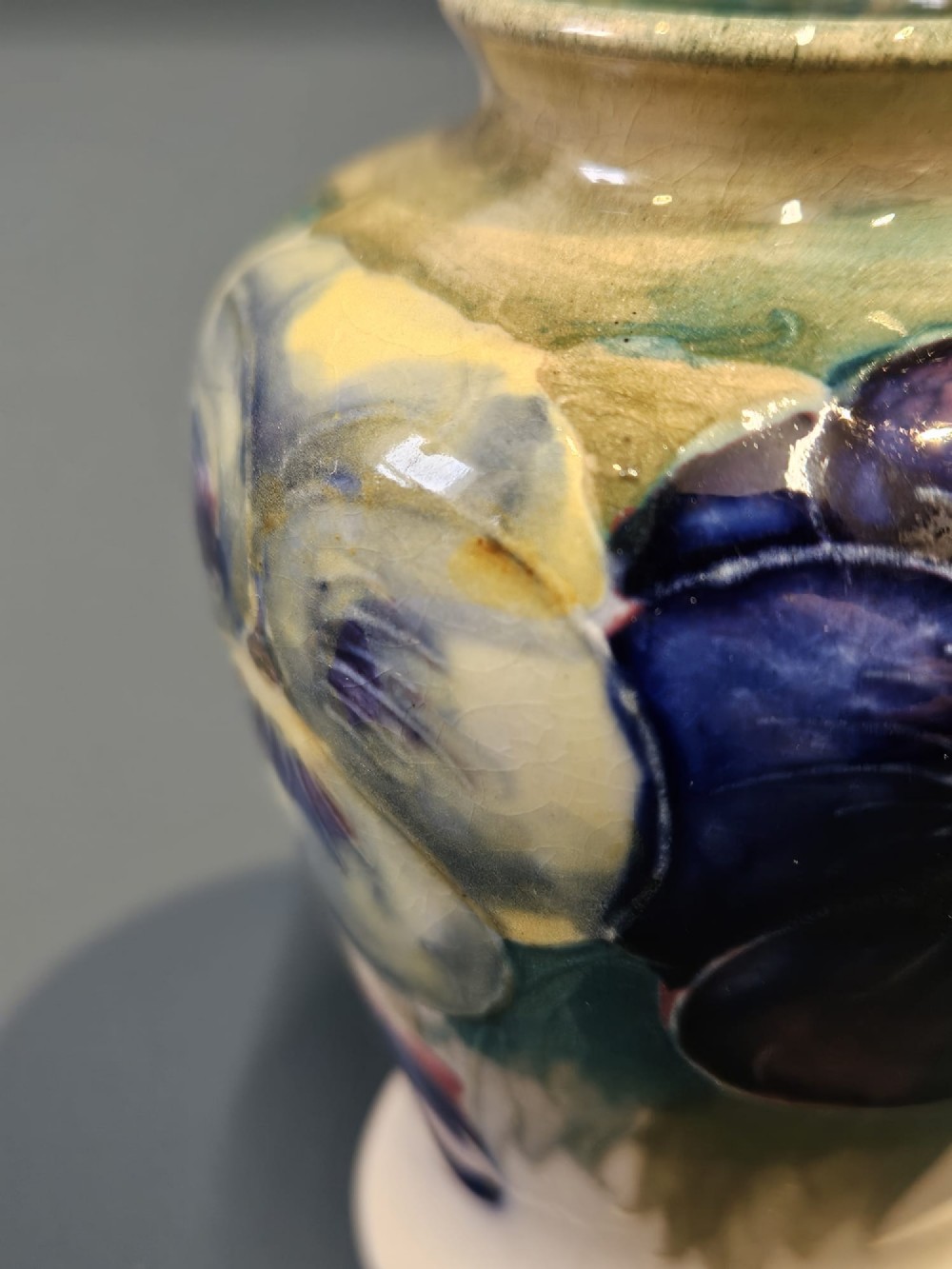 A small baluster-shaped ceramic vase decorated with hand-painted purple and blue pansies on a cream background with a flared green rim. View V