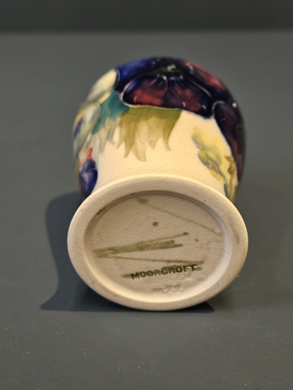 A small baluster-shaped ceramic vase decorated with hand-painted purple and blue pansies on a cream background with a flared green rim. View VI
