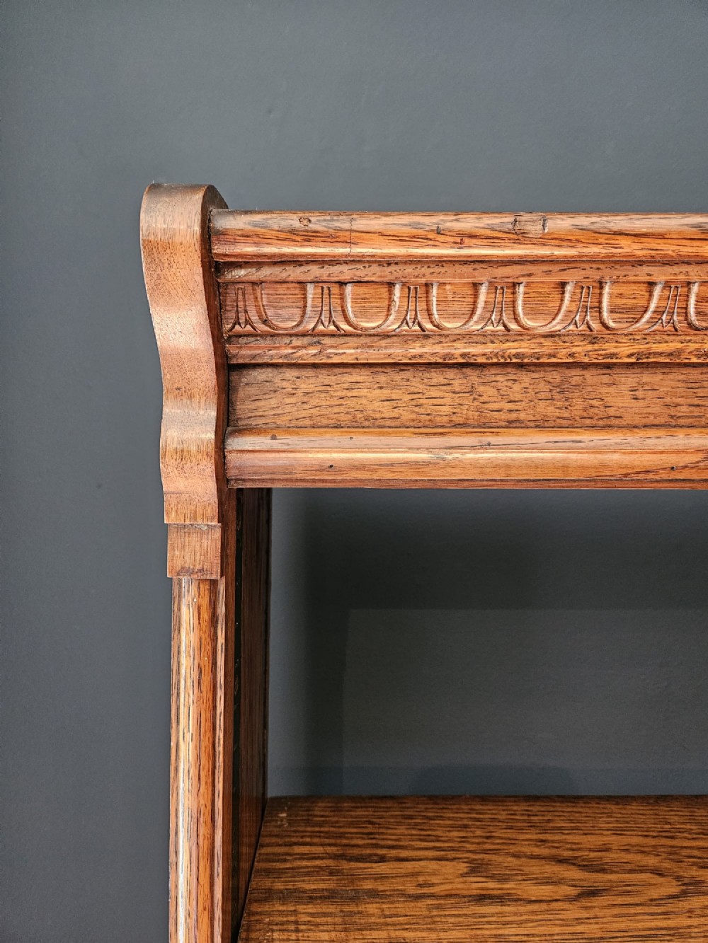 A tall Edwardian oak open bookcase featuring six tiers of shelving with carved egg and dart moulding along the top frieze. View II