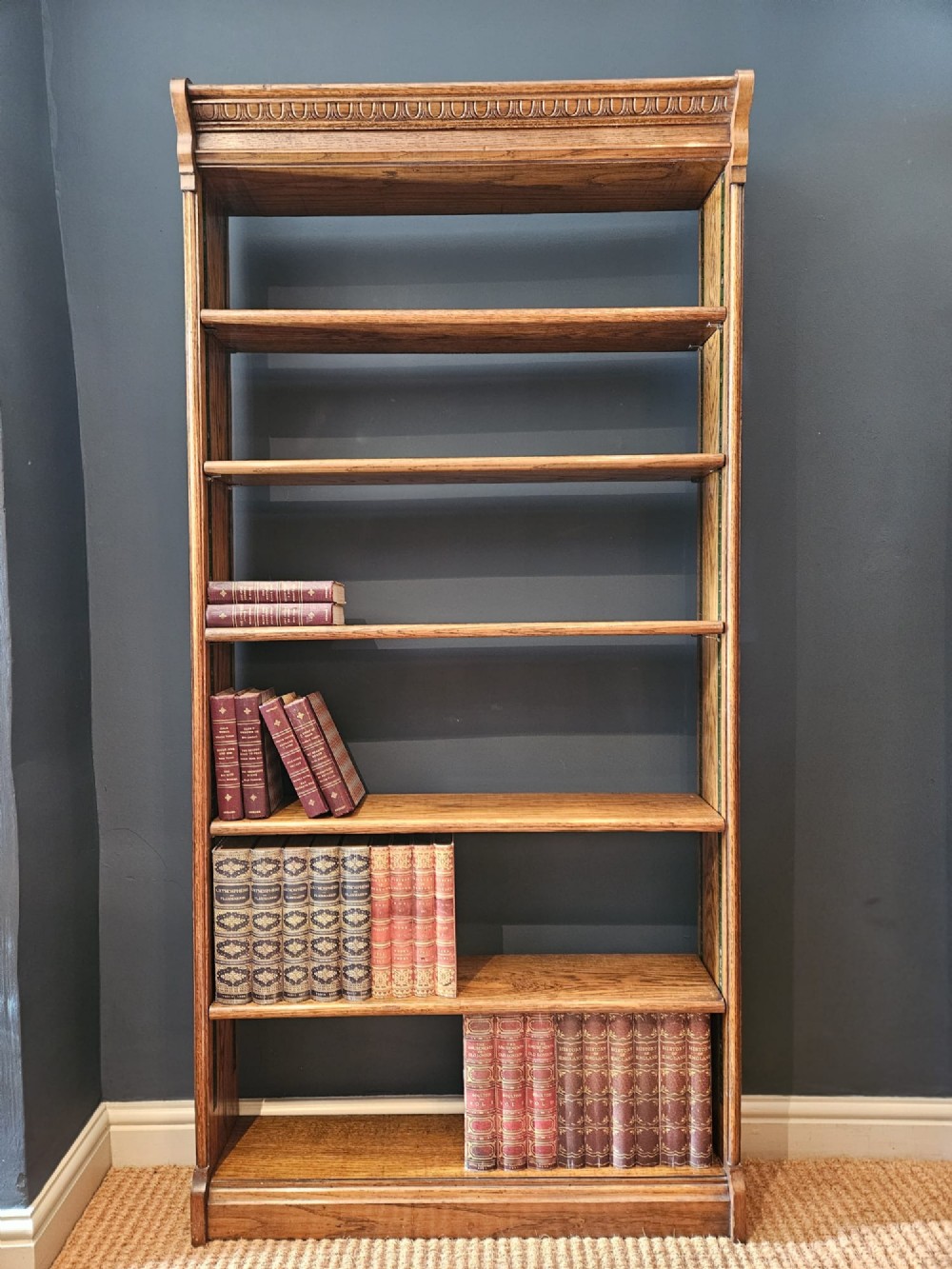 A tall Edwardian oak open bookcase featuring six tiers of shelving with carved egg and dart moulding along the top frieze. View IV
