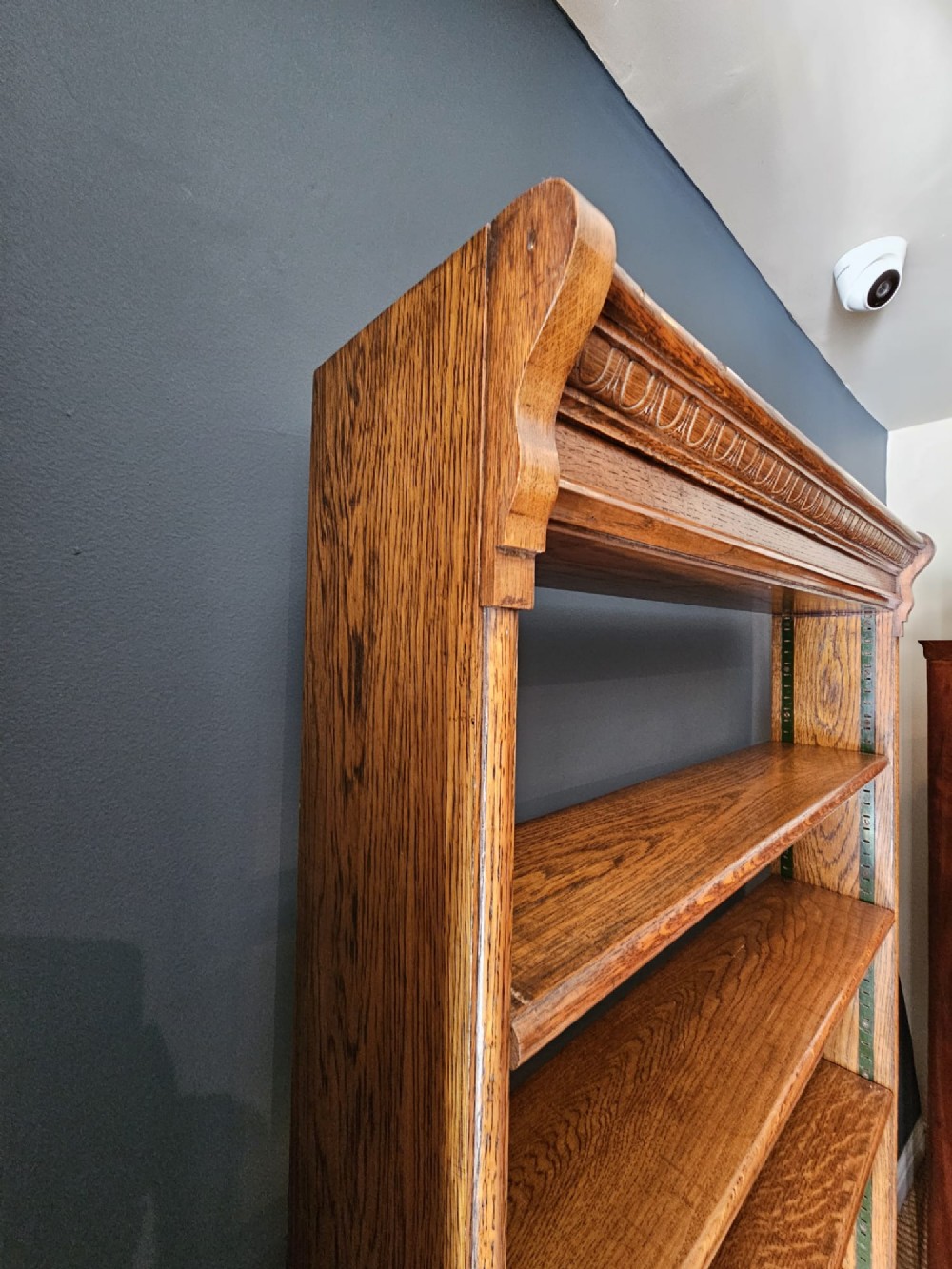 A tall Edwardian oak open bookcase featuring six tiers of shelving with carved egg and dart moulding along the top frieze. View VI