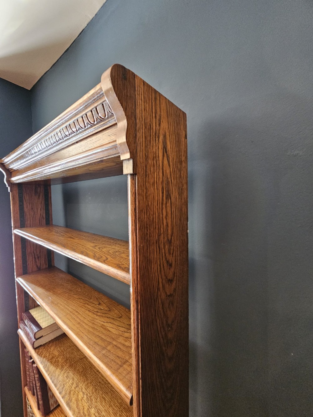A tall Edwardian oak open bookcase featuring six tiers of shelving with carved egg and dart moulding along the top frieze. View VII