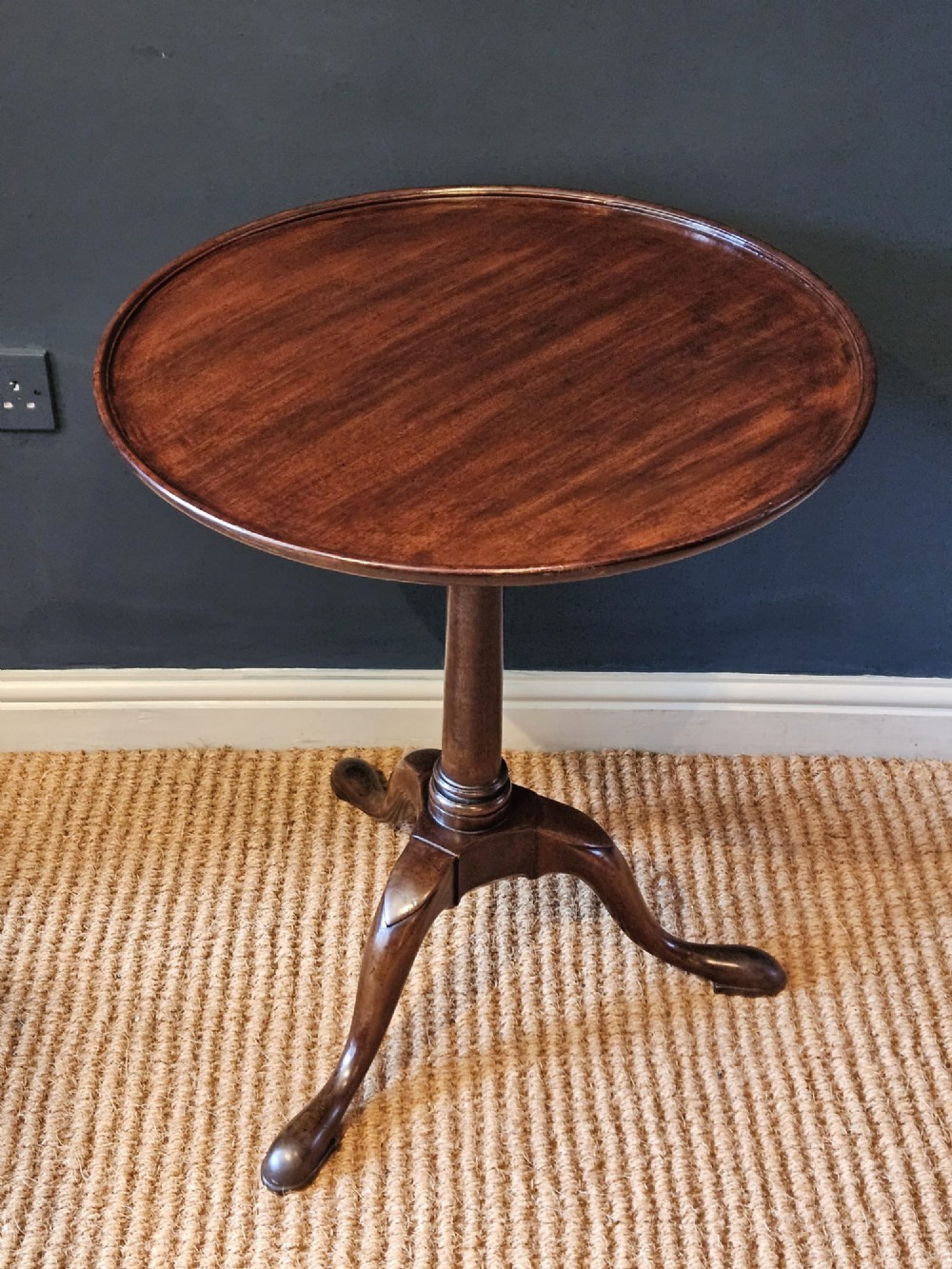 A George II red walnut tripod table featuring a circular dished top set upon a turned central column and three cabriole legs with pad feet. View II