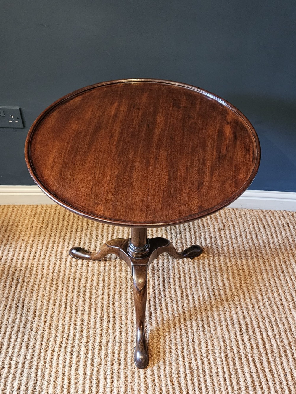 A George II red walnut tripod table featuring a circular dished top set upon a turned central column and three cabriole legs with pad feet. View V